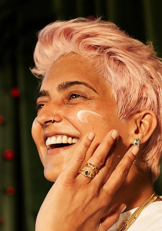 Smilende kvinne med rosa hår smører fuktighetskrem i ansiktet.