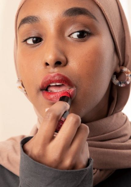 Kvinne med hijab påfører en rød leppestift.