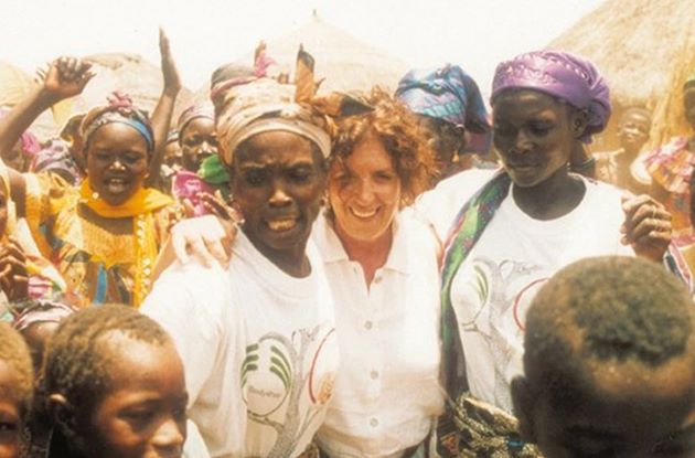 Dame Anita Roddick smiler og holder armene rundt to afrikanske kvinner