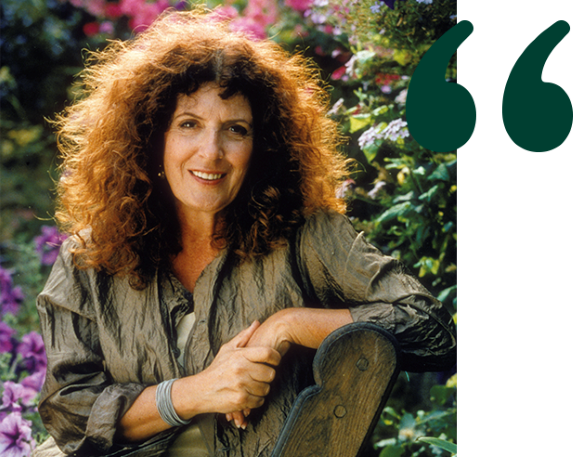 Anita Roddick sittende på en benk med blomster i bakgrunnen