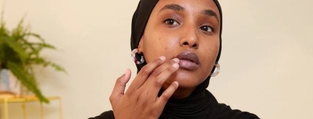 Kvinne med svart hijab som påfører leppeprodukt på leppene med fingeren. Foto